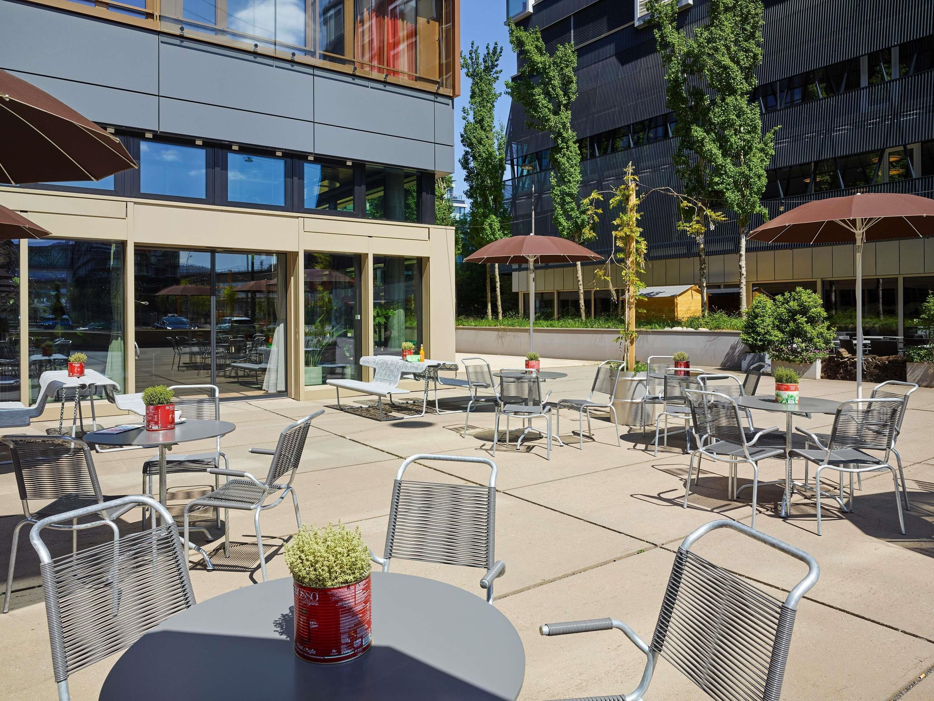 An outdoor seating area with tables and chairs, some with umbrellas, and potted plants.
