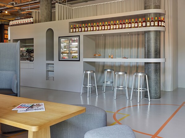 Un espace bar moderne, doté de tabourets, d’un réfrigérateur et d’étagères remplies de bouteilles.
