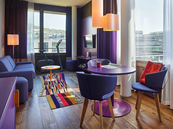 Une chambre d’hôtel moderne équipée d’un canapé, de fauteuils, d’une petite table, d’un tapis de course et offrant une vue sur la ville.
