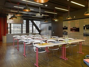 Un espace de restauration moderne, doté de tables et de chaises, d’un projecteur et offrant une vue sur la ville grâce à de grandes fenêtres.
