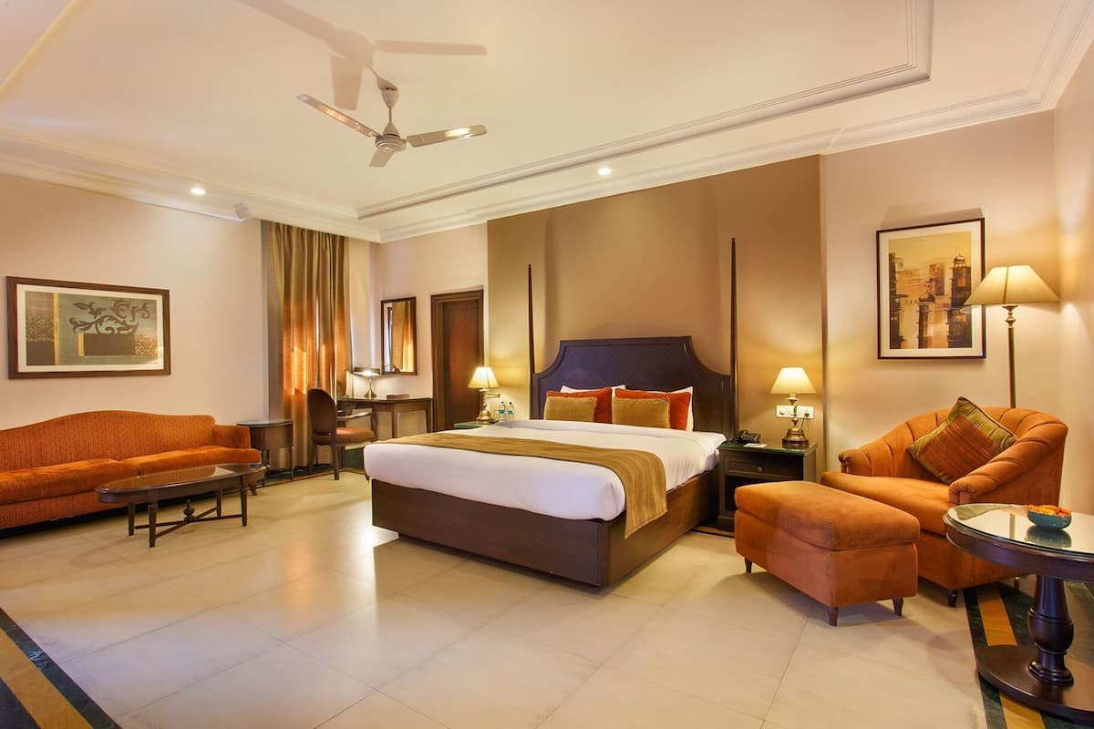A hotel room with a bed, two sofas, a desk, a chair, a lamp, and a ceiling fan.