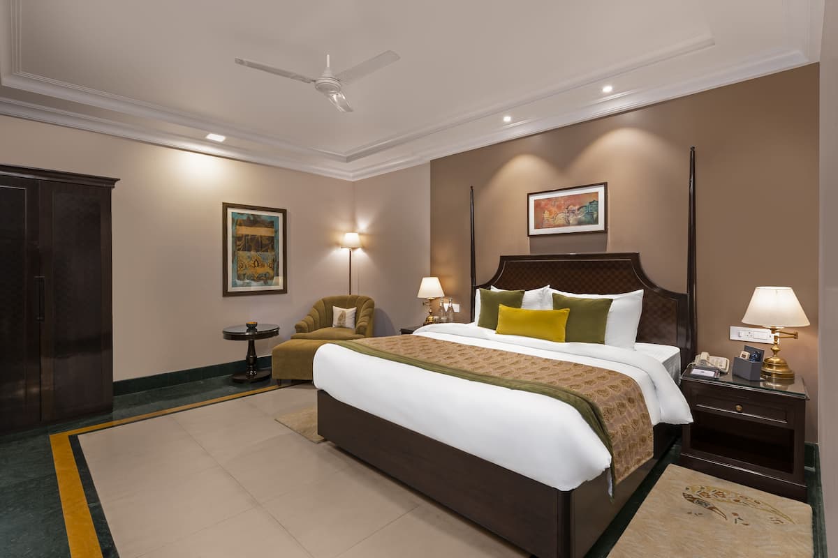 A hotel room with a large bed, two bedside tables with lamps, a chair, a wardrobe, and a ceiling fan.