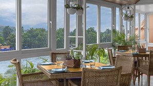 A dining area with wicker furniture, large windows, and a view of the water. - Ganga Lahari, Haridwar (Haridwar)