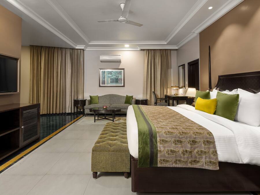 A hotel room with a large bed, a sofa, a TV, and a ceiling fan.