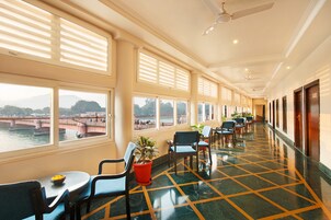 A hotel corridor with a view of a river and bridge, chairs, tables, and potted plants.