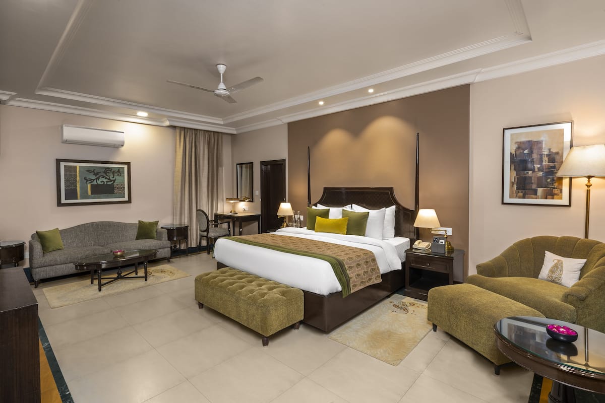 A hotel room with a bed, a sofa, a chair, a small table, and a desk.