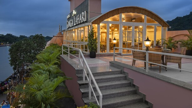 A hotel with a large sign, a covered outdoor area with seating, and a view of the water. - Ganga Lahari, Haridwar (Haridwar)