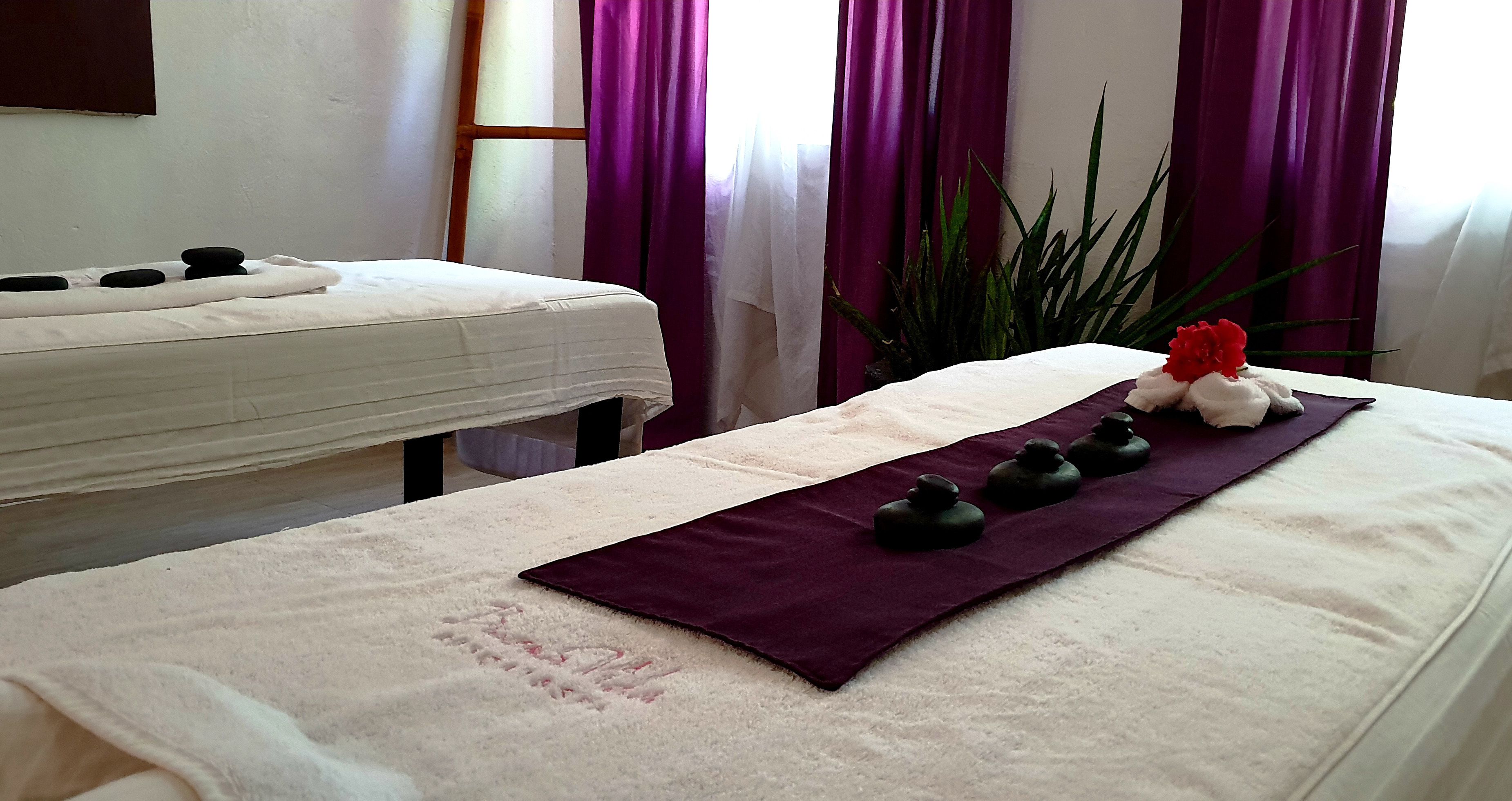 A massage therapy room with two massage tables, each with a white towel and black stones.