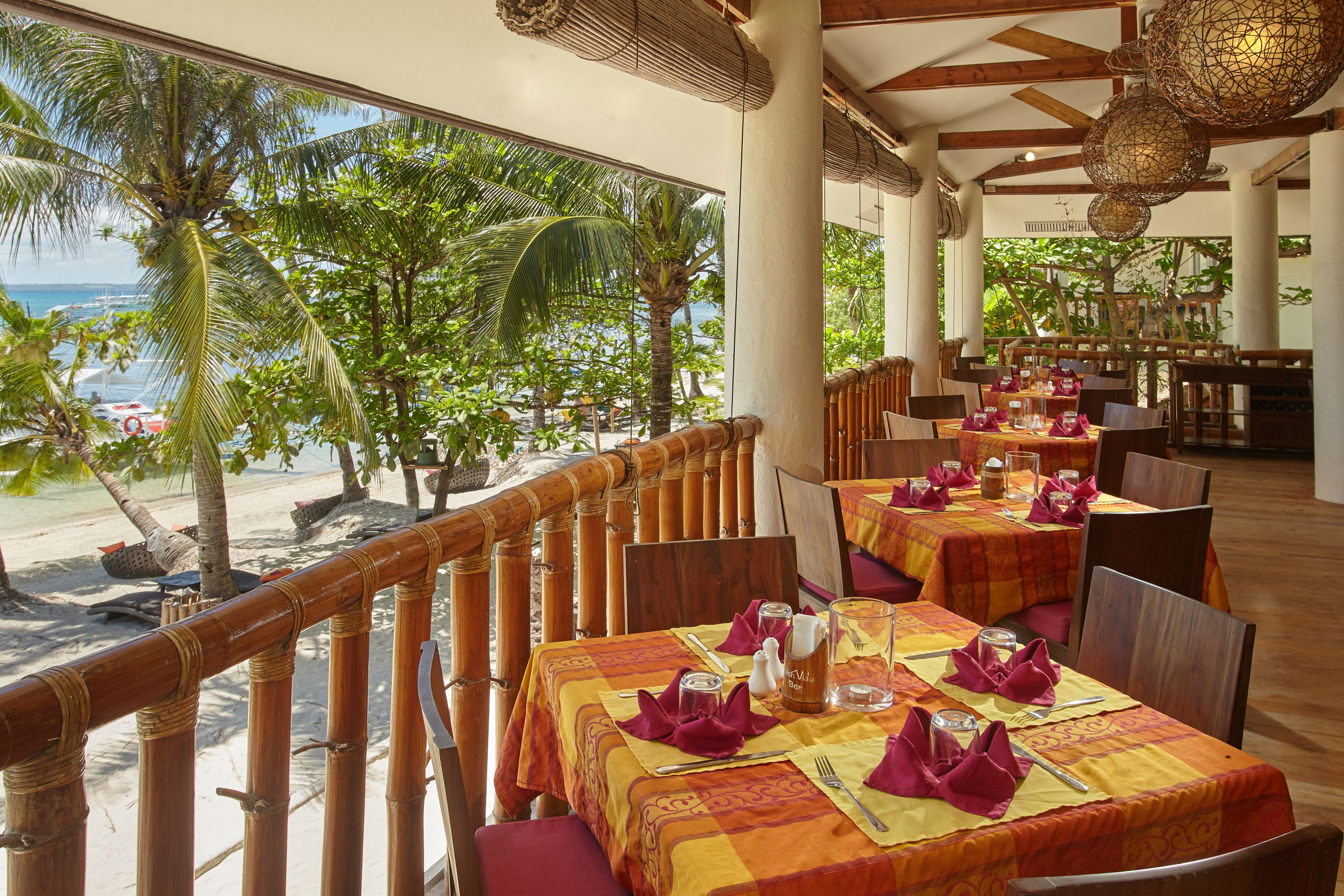 A restaurant with tables set for dining, overlooking a beach with palm trees.