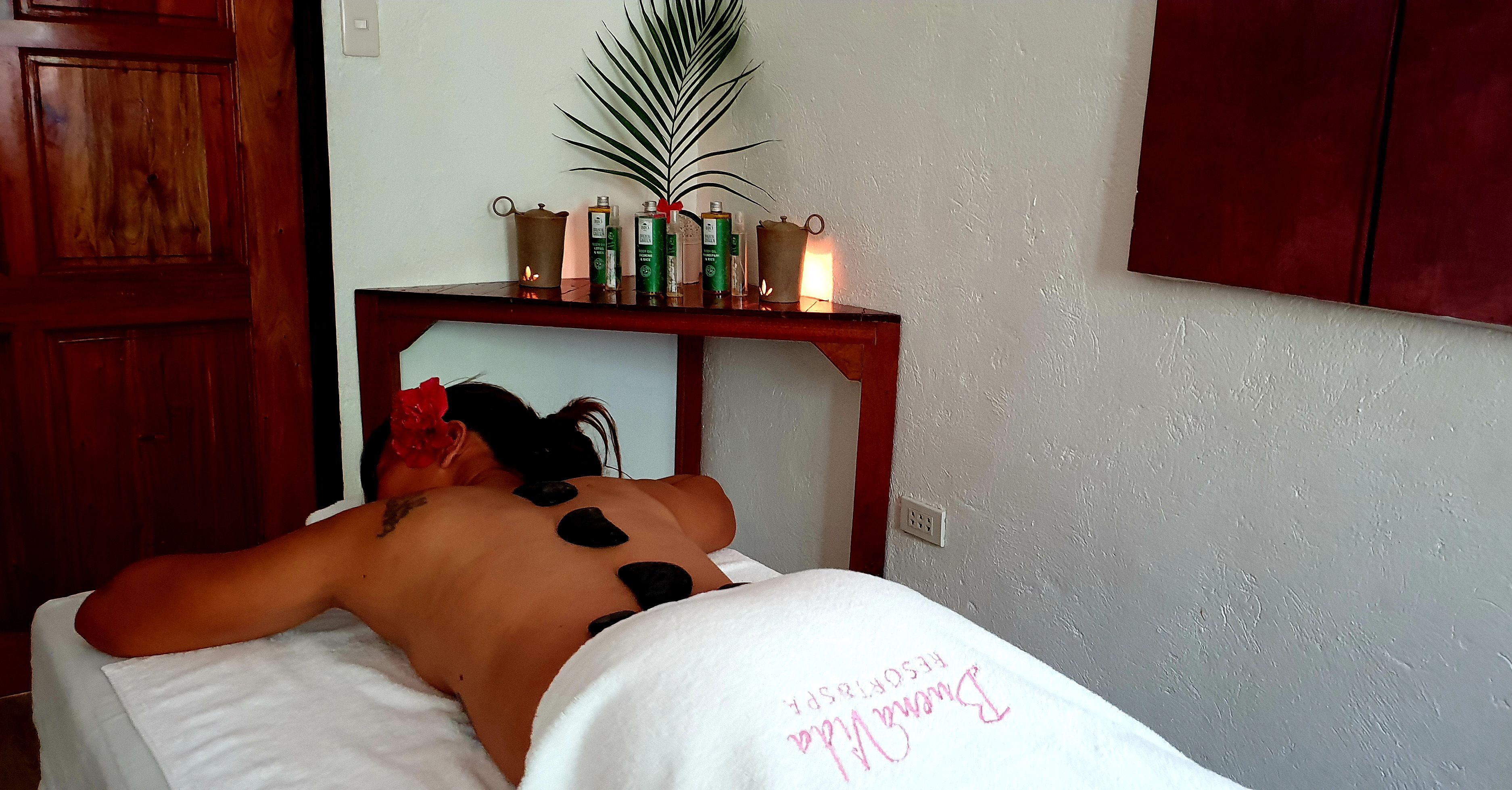 A massage therapy room with a wooden cabinet, a shelf with candles, and a white towel on the bed.