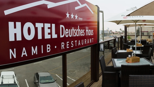 Blick auf das Hotel Deutsches Haus Namib Restaurant mit Außenplätzen und Sonnenschirmen.