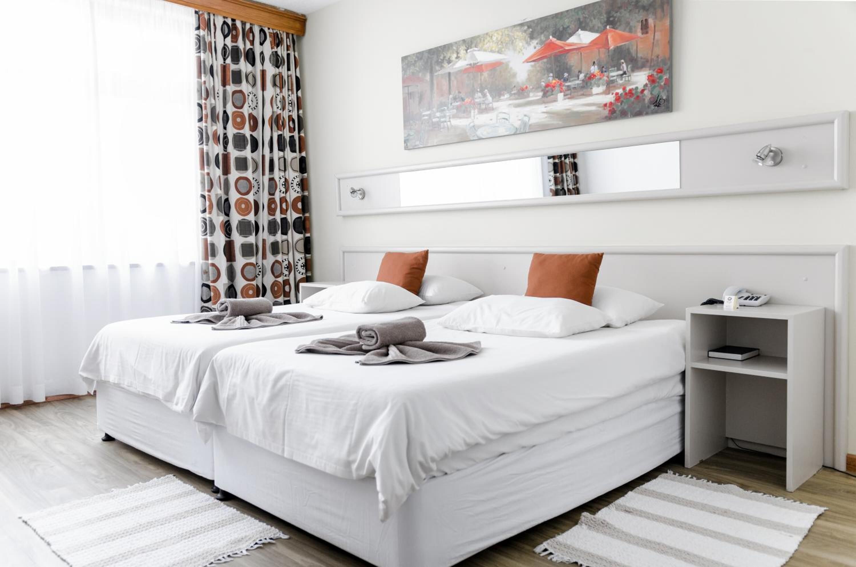 A neatly arranged double bed with white bedding and brown pillows, a bedside table with a phone, and a painting above the bed.