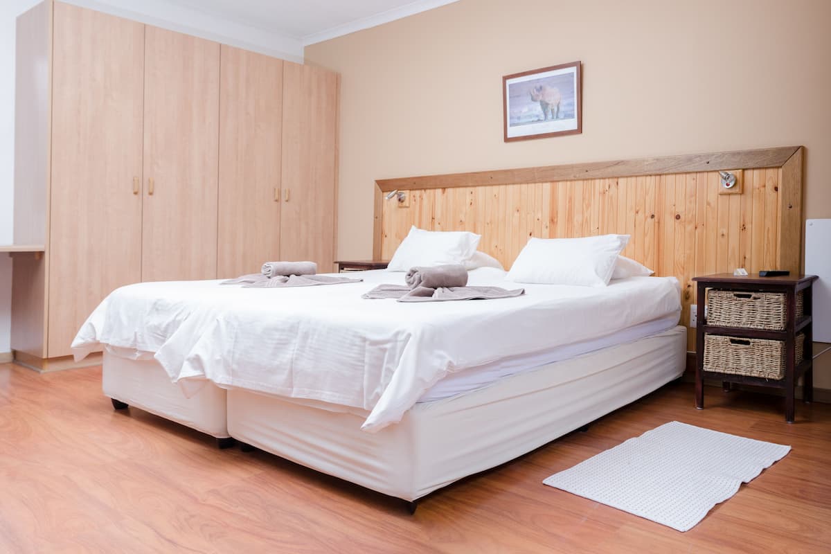 Un dormitorio con cabecera de madera, cama con ropa de cama blanca, armario de madera y un cuadro en la pared.