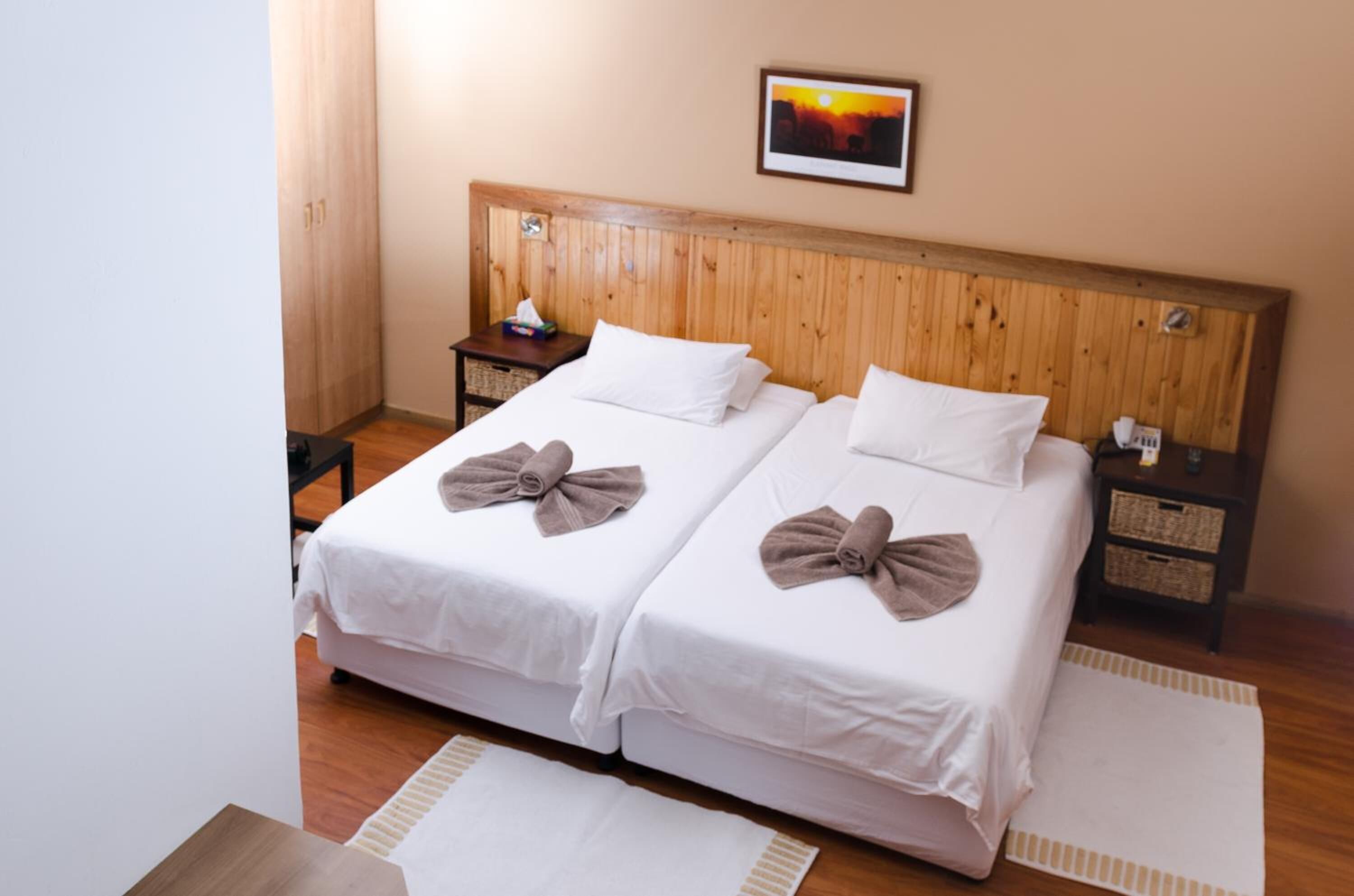 Ein Doppelzimmer mit zwei Betten, einem Holzkopfteil, Nachttischen und einem Wandbild.