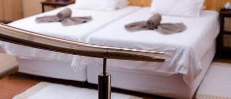 Una habitación de hotel con dos camas, cabecero de madera, ropa de cama blanca y una baranda metálica.