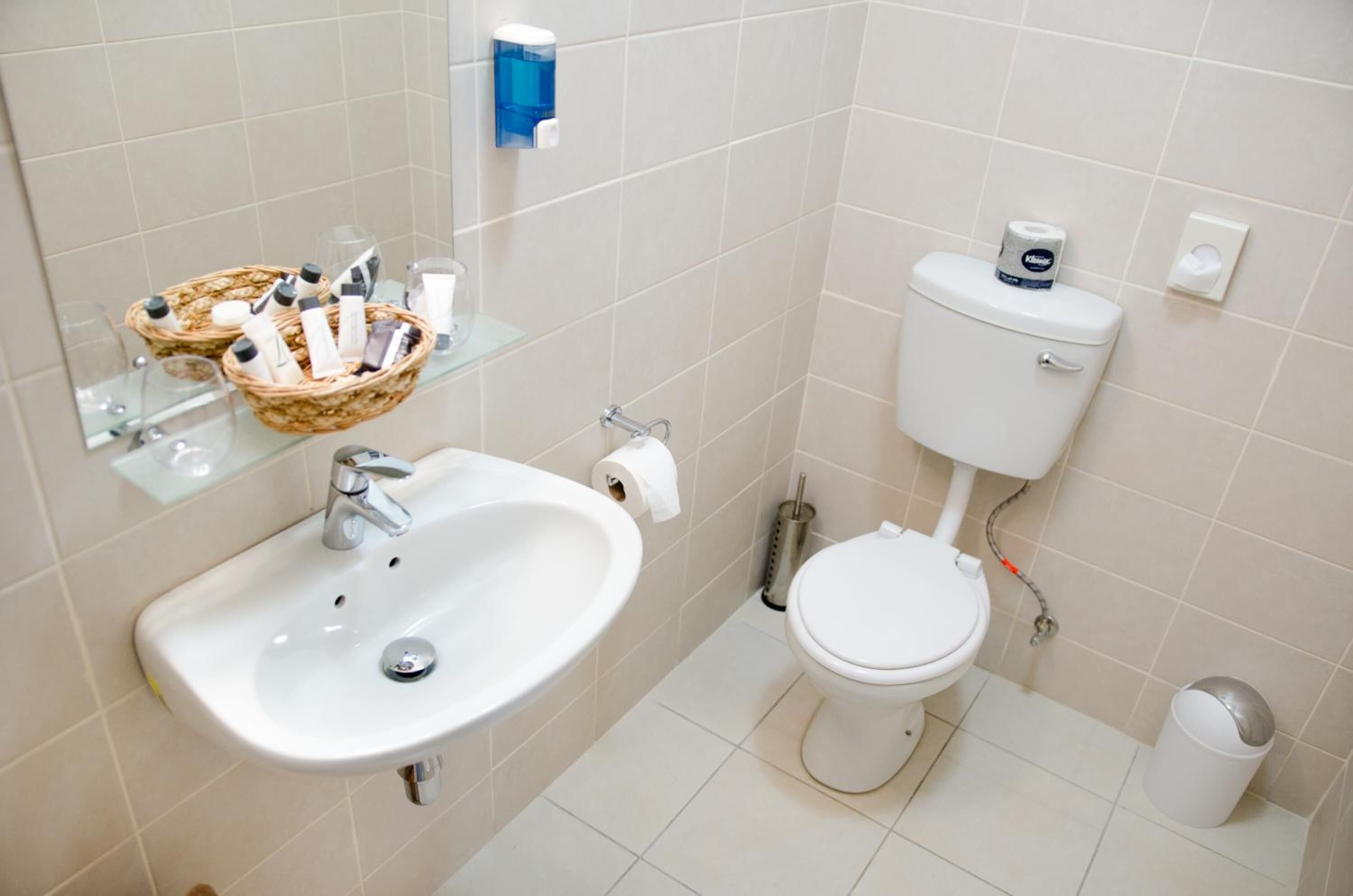Un baño con lavamanos, inodoro y una cesta de artículos de aseo.