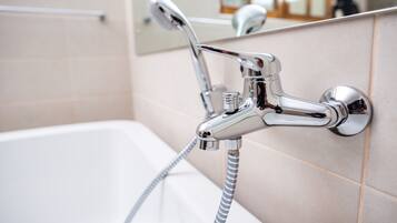 Un cabezal de ducha cromado con una manguera flexible, fijado a una pared con azulejos.