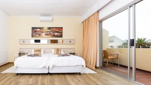 Ein Schlafzimmer mit zwei Betten, einem großen Fenster mit Vorhängen, einem Gemälde über den Betten und Blick ins Freie.