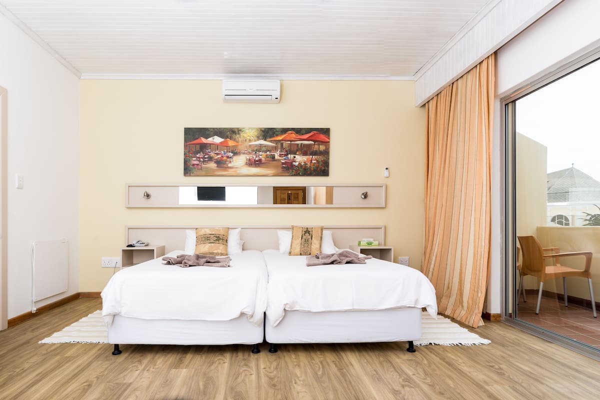 Un dormitorio con dos camas, un ventanal con cortinas, un cuadro sobre las camas y vistas al exterior.