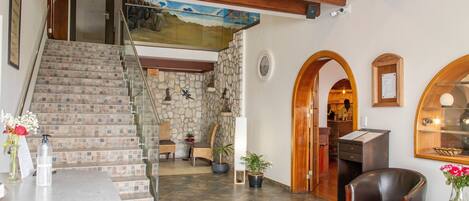 Una escalera con escalones de piedra, techo de madera, comedor con sillas y mesa, y mostrador de recepción.