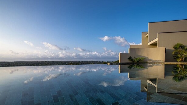 A modern infinity pool reflecting the sky and clouds, with a clear view of the horizon and distant landscape.