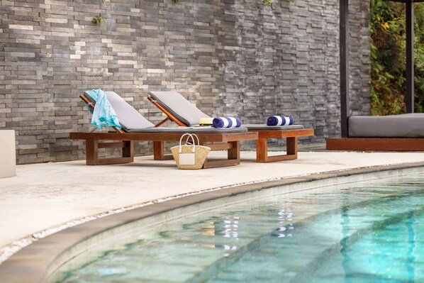 Un área junto a la piscina con dos sillones de madera, una mesita y una cesta de mimbre.