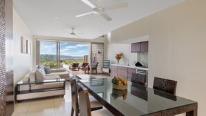 A modern living room with a glass dining table, a sofa, and a view of the outdoors.