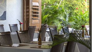 A dining area with wicker chairs and a table set for a meal, overlooking a lush garden.