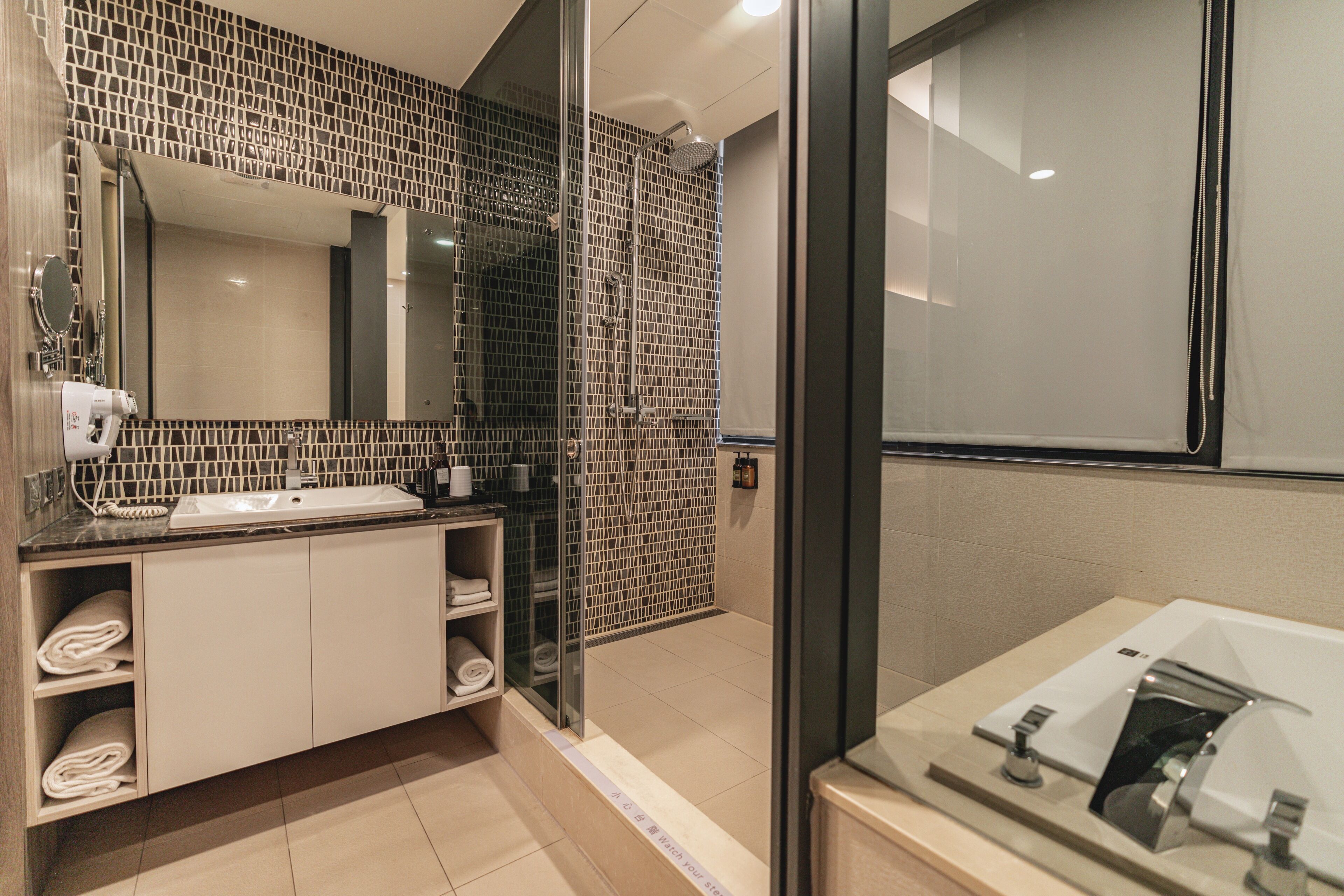 Un baño moderno con ducha de vidrio, un espejo grande y un lavamanos con toallero.