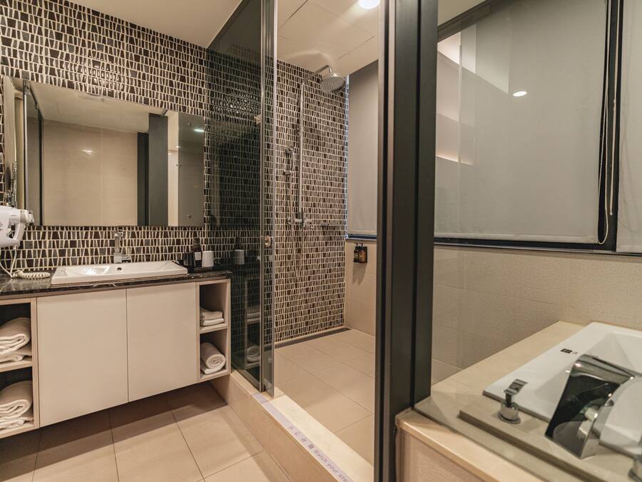Un baño moderno con ducha de vidrio, un espejo grande y un lavamanos con toallero.