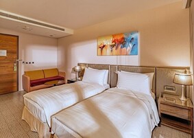 Habitación de hotel con dos camas, un sofá, un cuadro y una mesita de noche con lámpara.