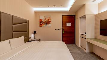 Hotelkamer met een groot bed, een bureau met een flatscreen televisie, een houten deur en een schilderij aan de muur.