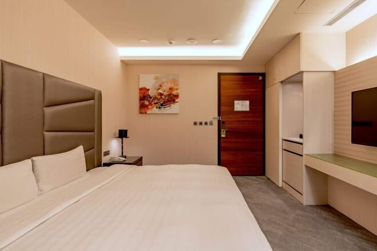 A modern hotel room with a large bed, a desk, a TV, and a door.
