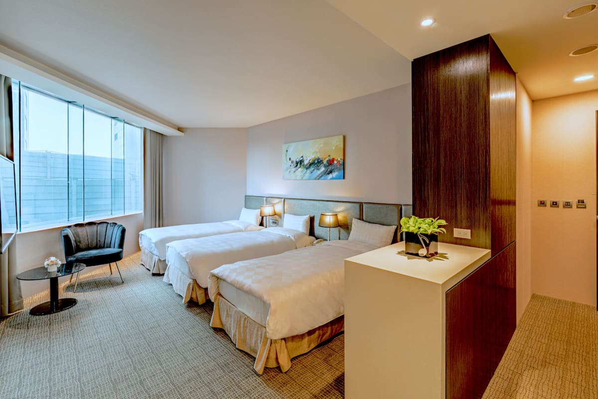 A hotel room with two beds, a desk, a chair, and a large window.