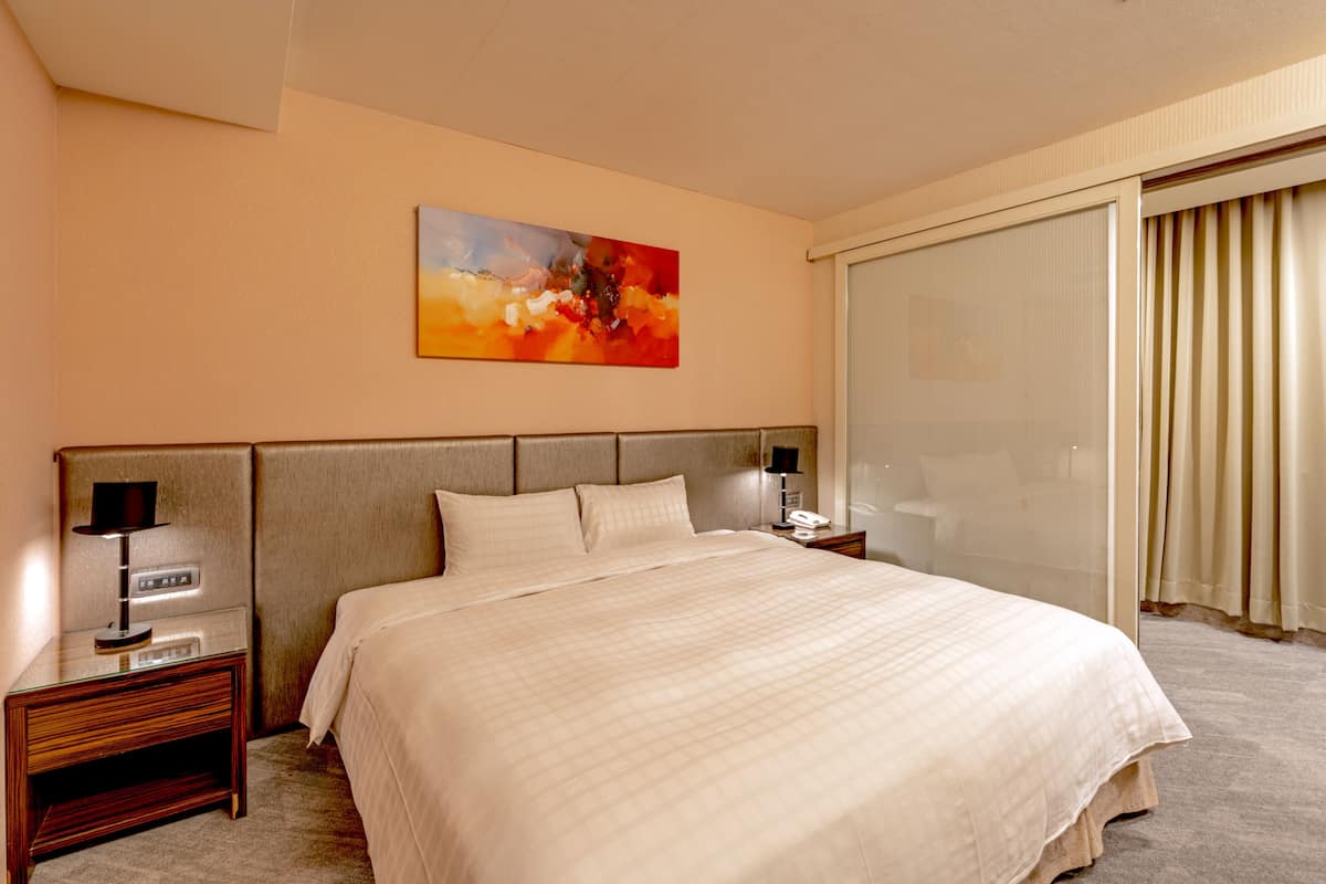A hotel room with a large bed, a nightstand with a lamp, a painting on the wall, and a sliding glass door.