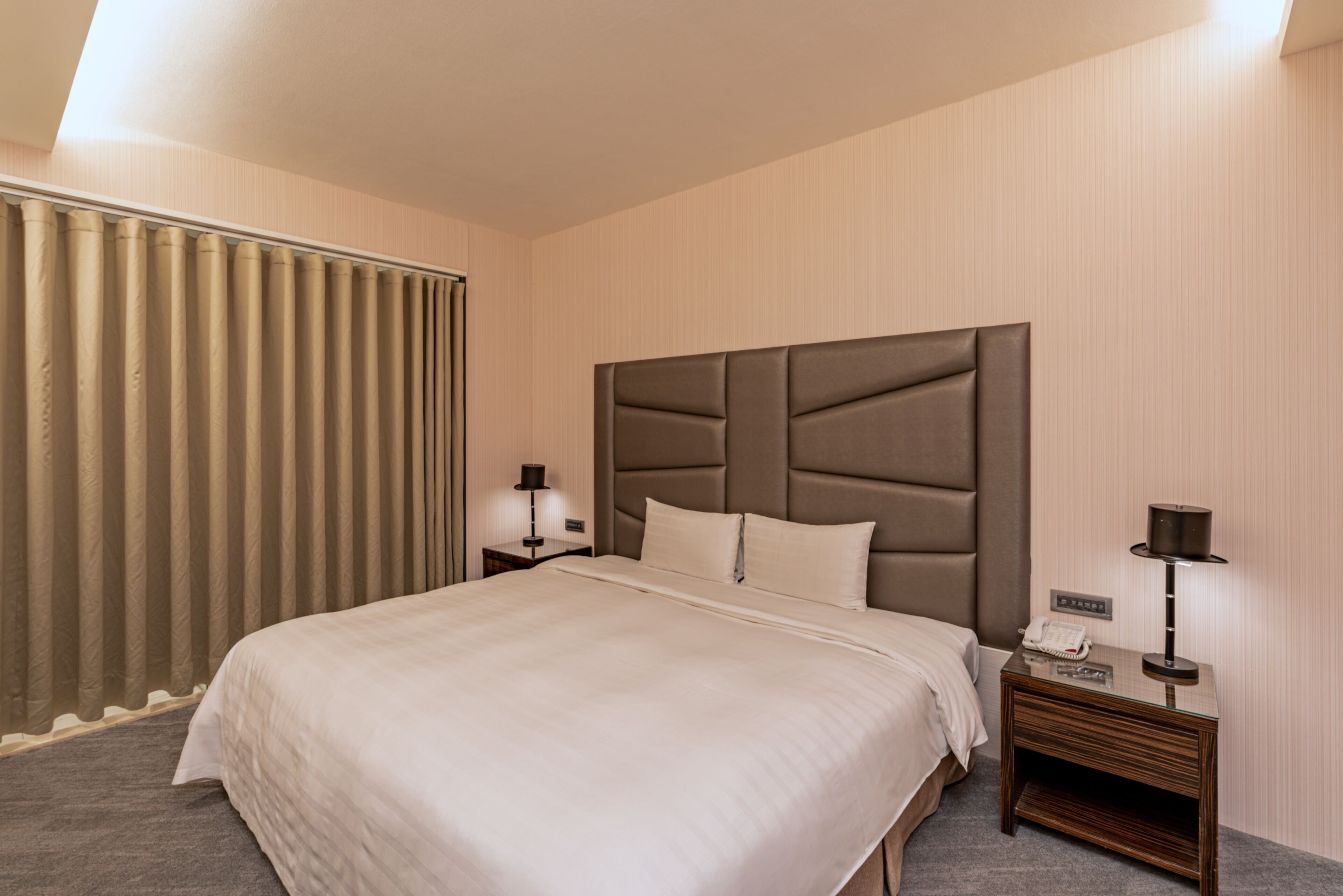 A hotel room with a large bed, a nightstand with a lamp, and a window with curtains.