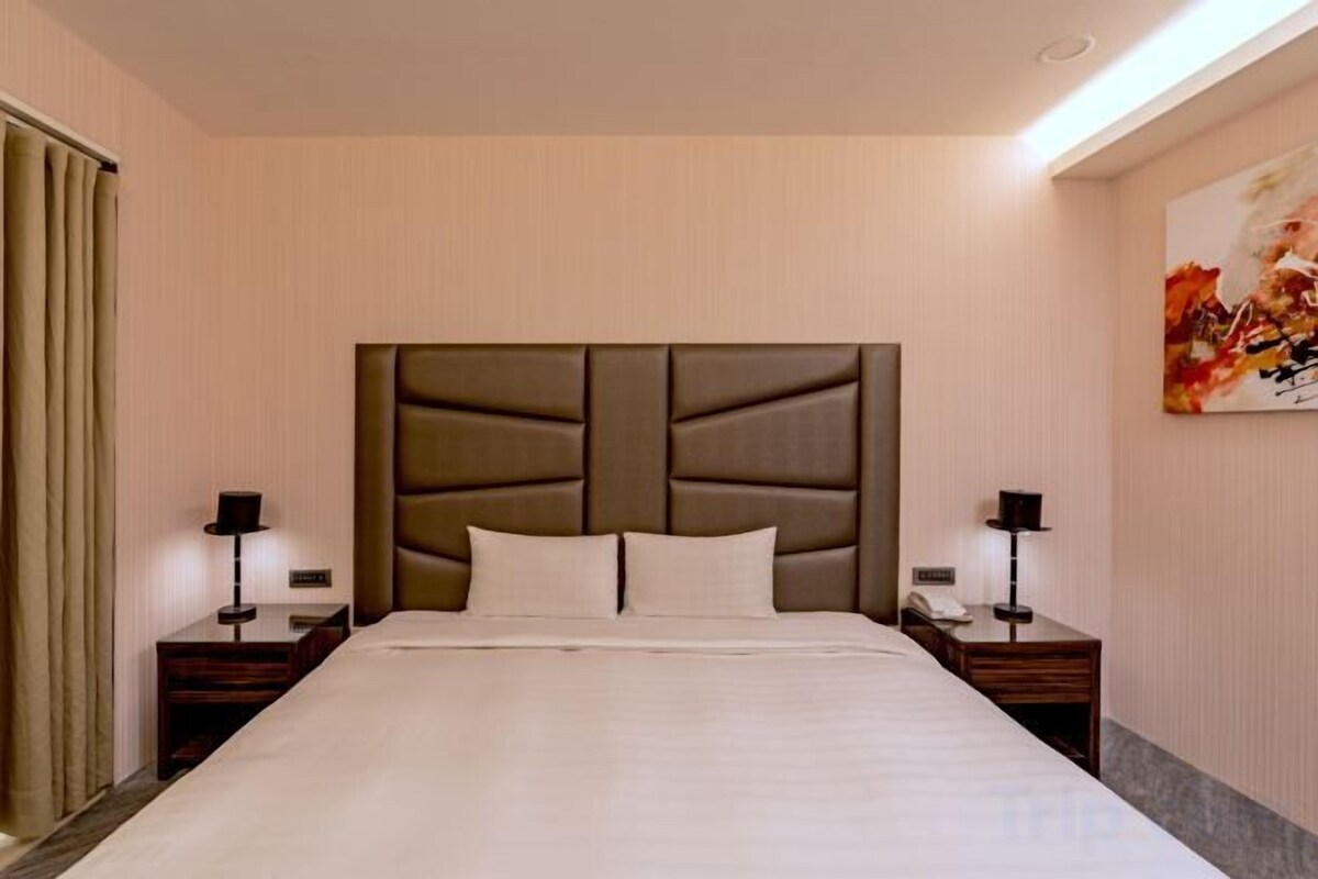 A hotel room with a large bed, two bedside tables, a headboard, and a painting on the wall.