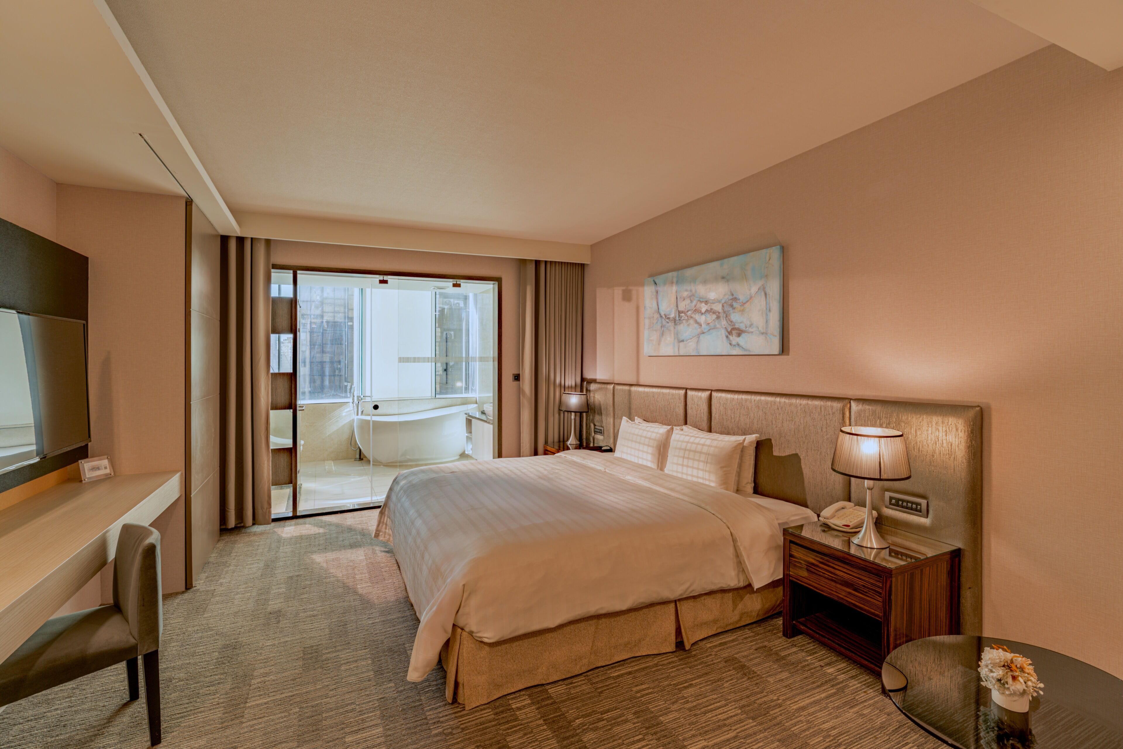 Habitación de hotel con una cama grande, un escritorio, una silla, una mesita de noche y vistas a la ciudad a través de la ventana.