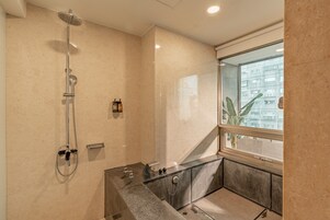 A modern bathroom with a shower, a vanity, and a window providing a view of buildings.