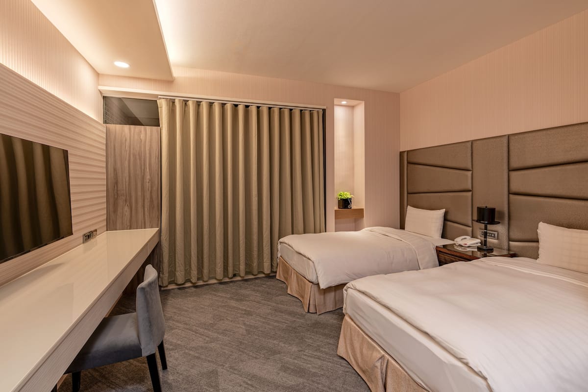 A hotel room with a desk, two beds, a nightstand, and a large mirror.