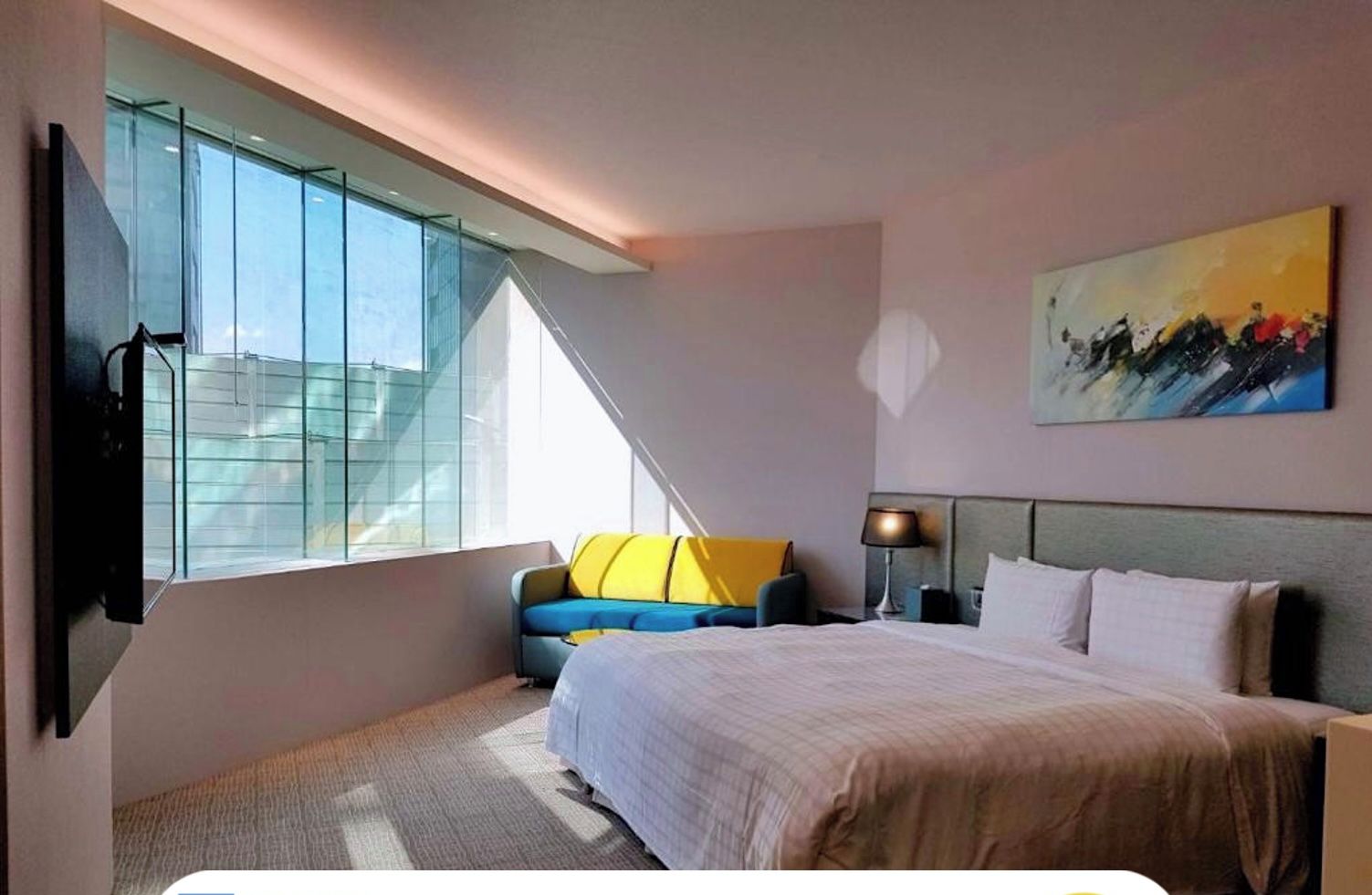 A modern hotel room with a large bed, a sofa, a TV, and a painting on the wall.