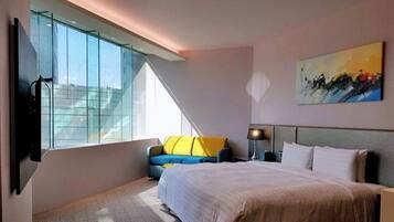 A modern hotel room with a large bed, a sofa, a TV, and a painting on the wall.