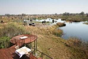 A dining area with a table and chairs overlooking a natural landscape with water and wildlife. - Nkasa Lupala Tented Lodge (Sangwali)