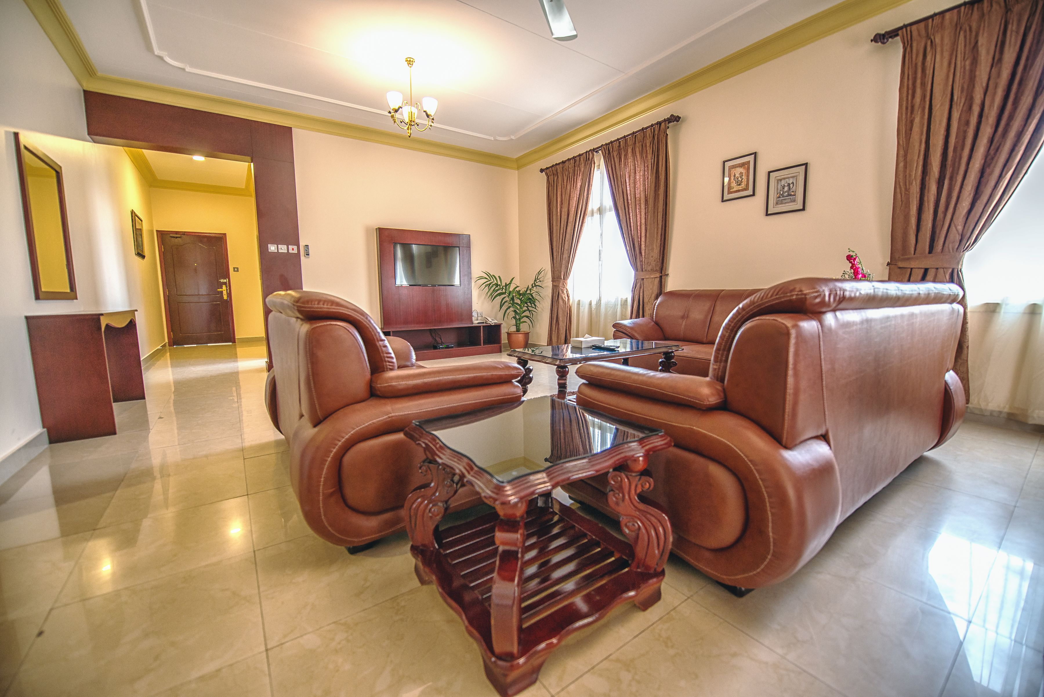 Un salón con un sofá de cuero marrón, una mesa de centro de cristal y una mesita auxiliar de madera.