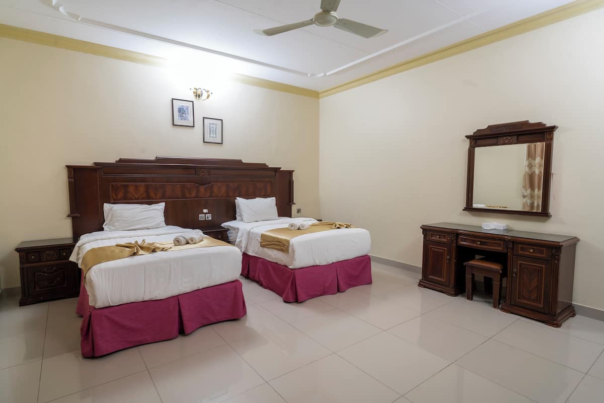 Habitación de hotel con dos camas, un escritorio, un espejo y un ventilador de techo.