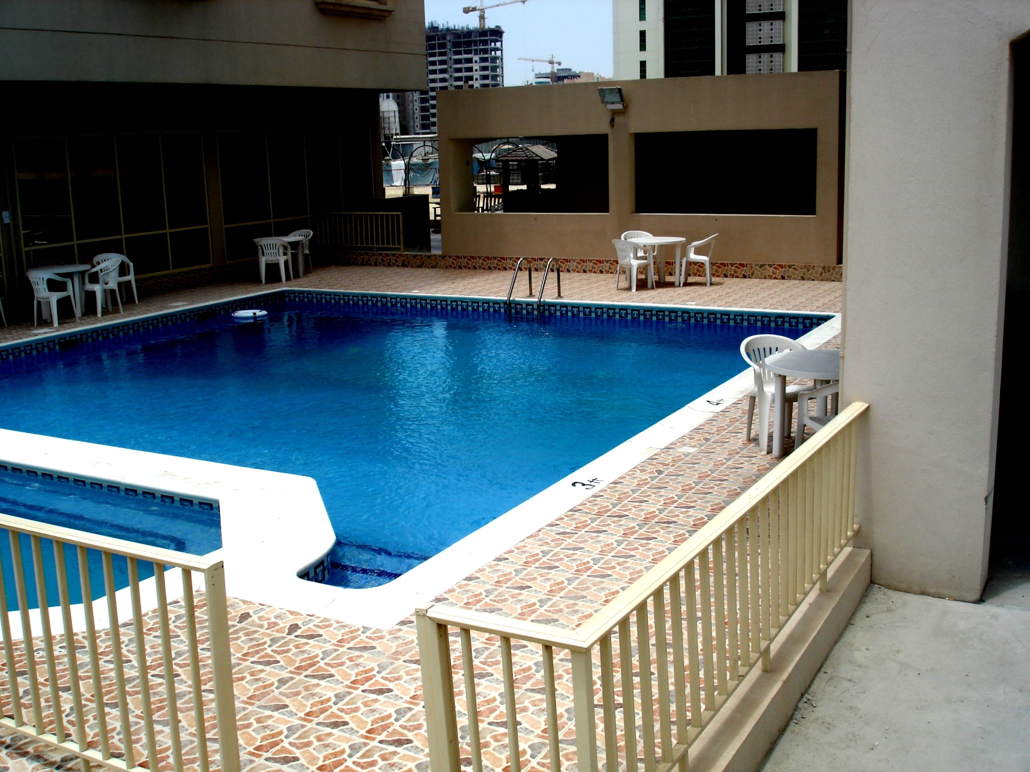 Una piscina con un borde de baldosas, rodeada de sillas blancas y una mesa pequeña.