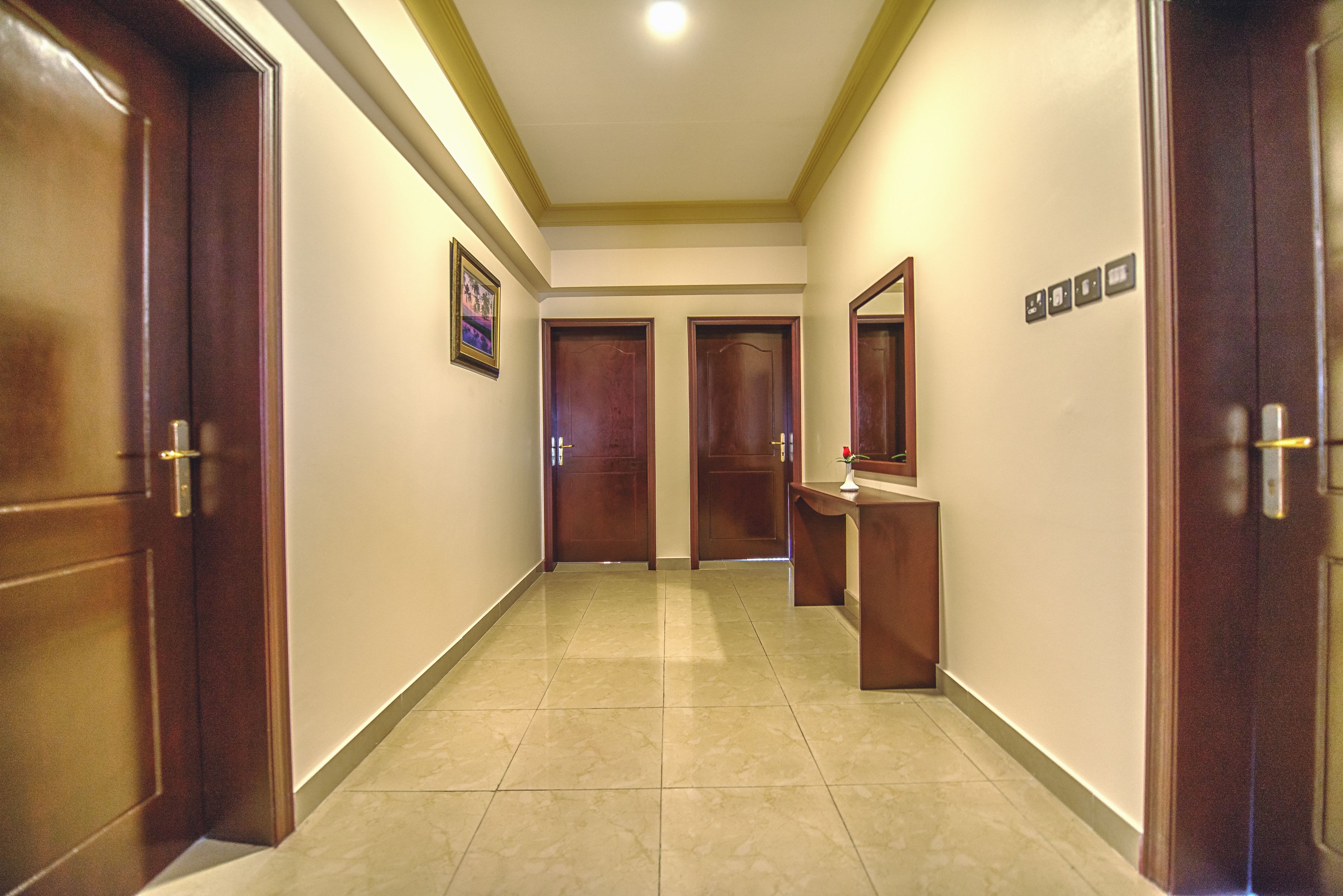 Un pasillo con puertas de madera, suelo de baldosas y un cuadro en la pared.
