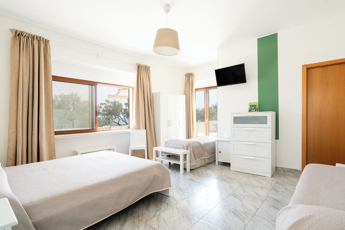 Quarto de hotel com duas camas, televisão, escrivaninha e janela com cortinas.