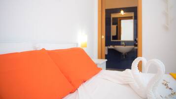 Quarto de hotel com cama, almofadas laranja, toalha branca e decoração em formato de coração.