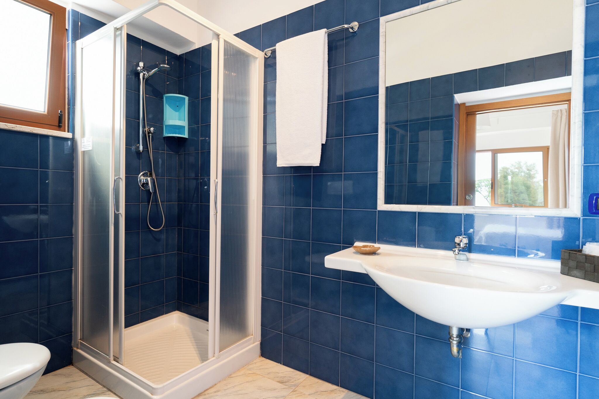 A bathroom with a glass-enclosed shower, a white sink, and blue-tiled walls.